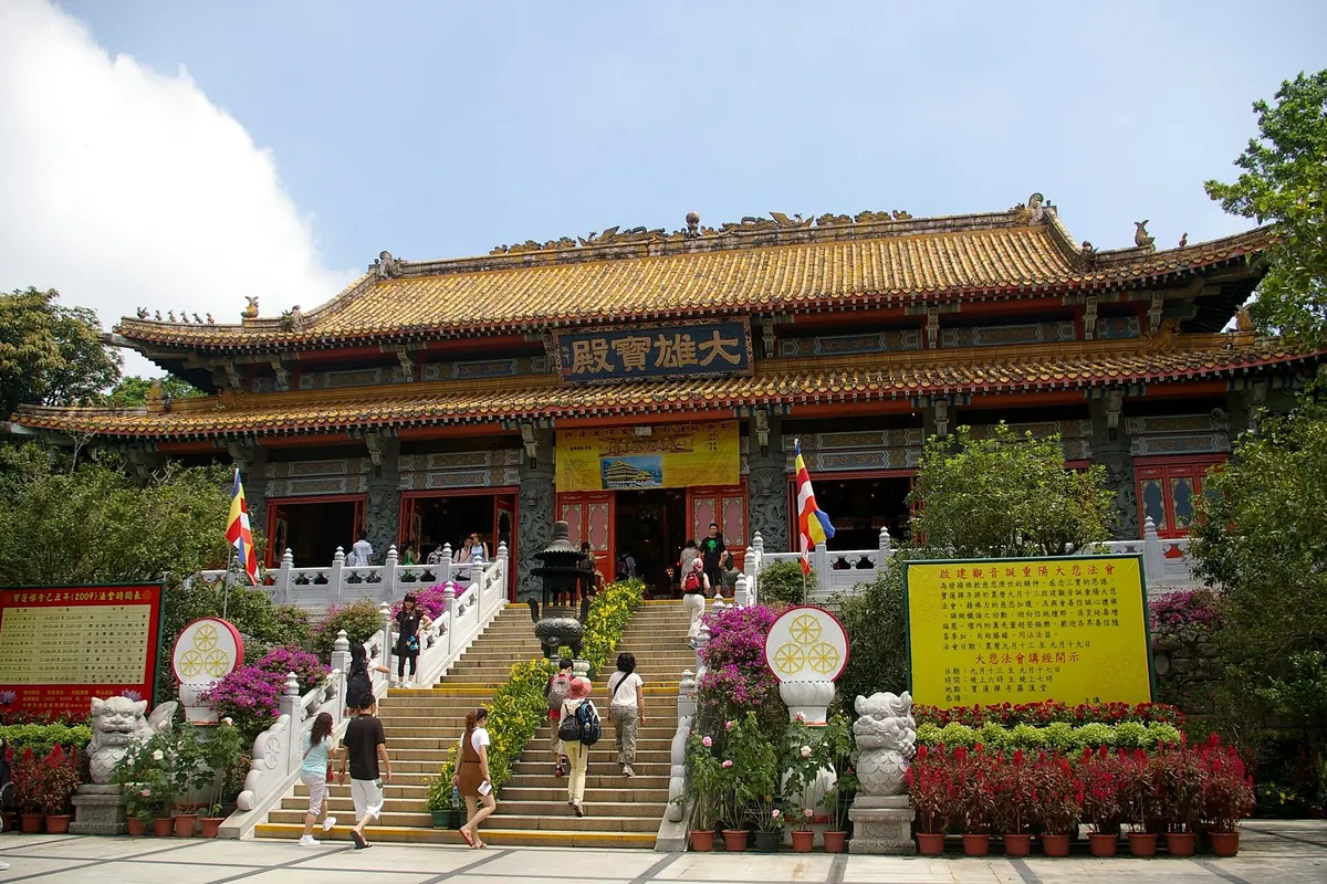 The main hall of Po Lin Monastery with a yellow-tiled roof and red pillars, reached by a wide white staircase with flower beds on each side